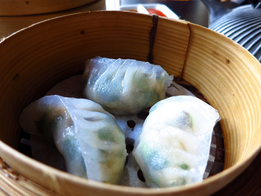 Três bolinhos translúcidos cozidos no vapor dentro de uma cesta de bambu.