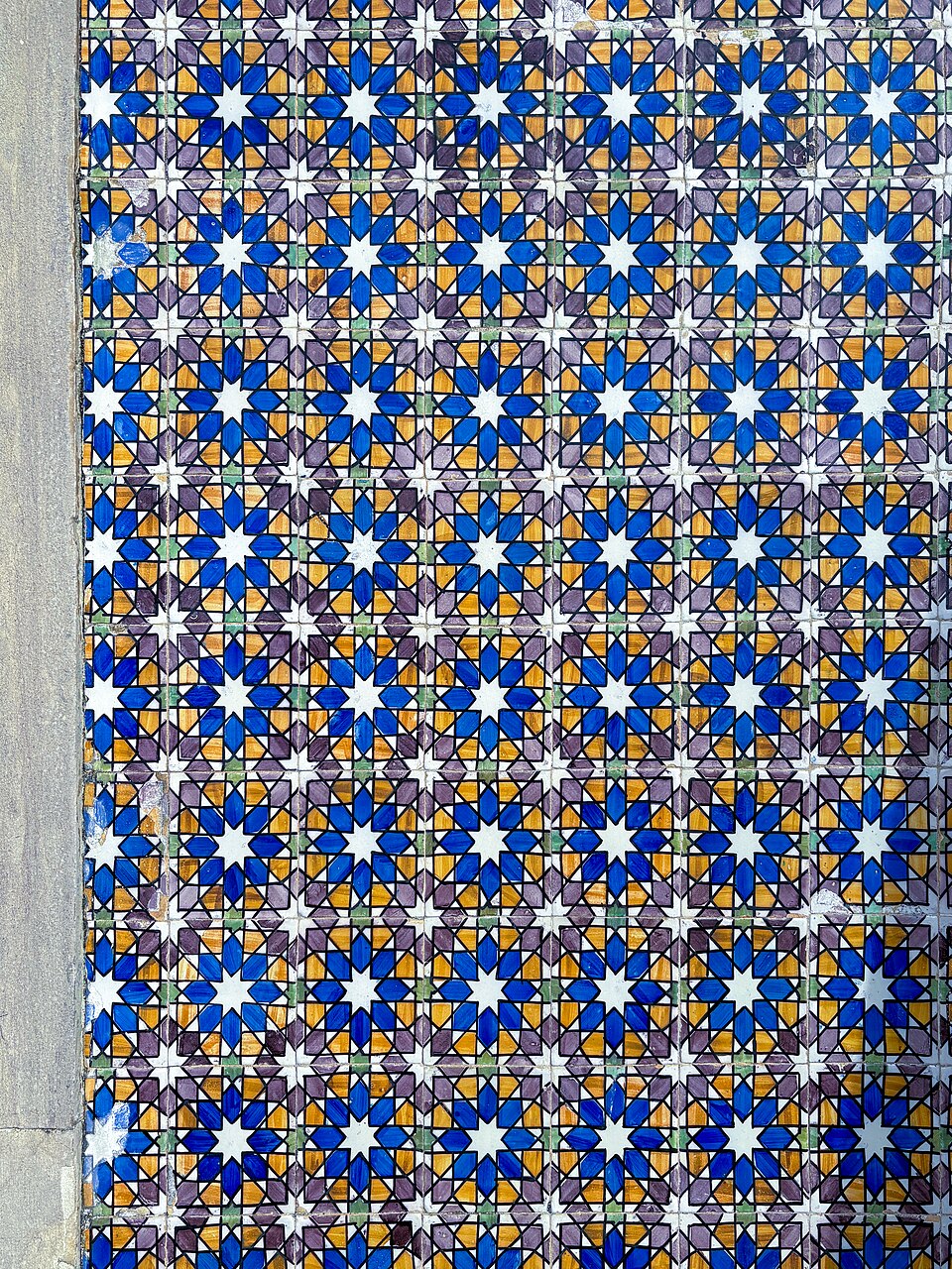 Painel de azulejos com padrões geométricos em azul, branco e dourado.
