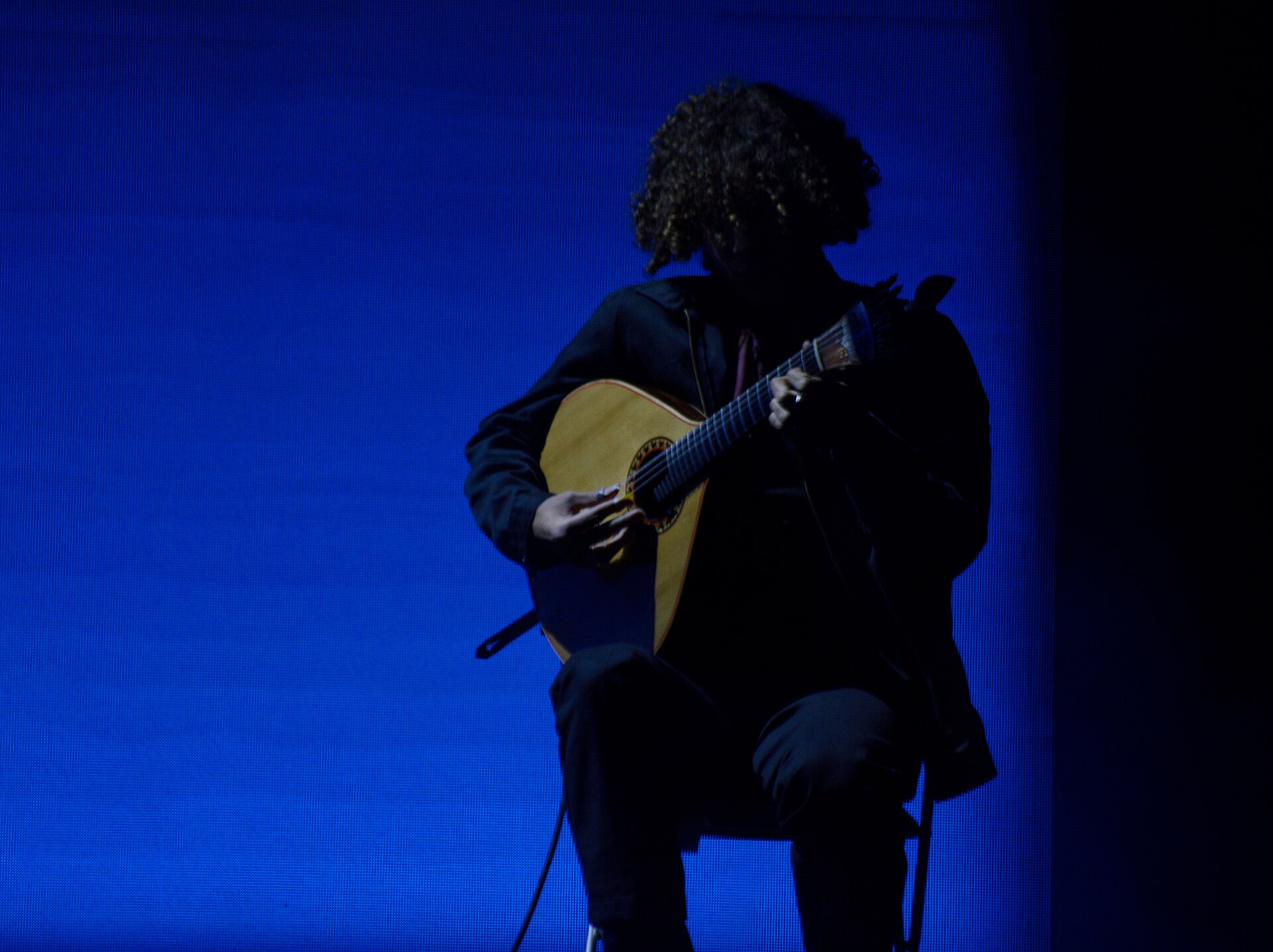 Gaspar Varela toca guitarra portuguesa em um palco iluminado de azul.