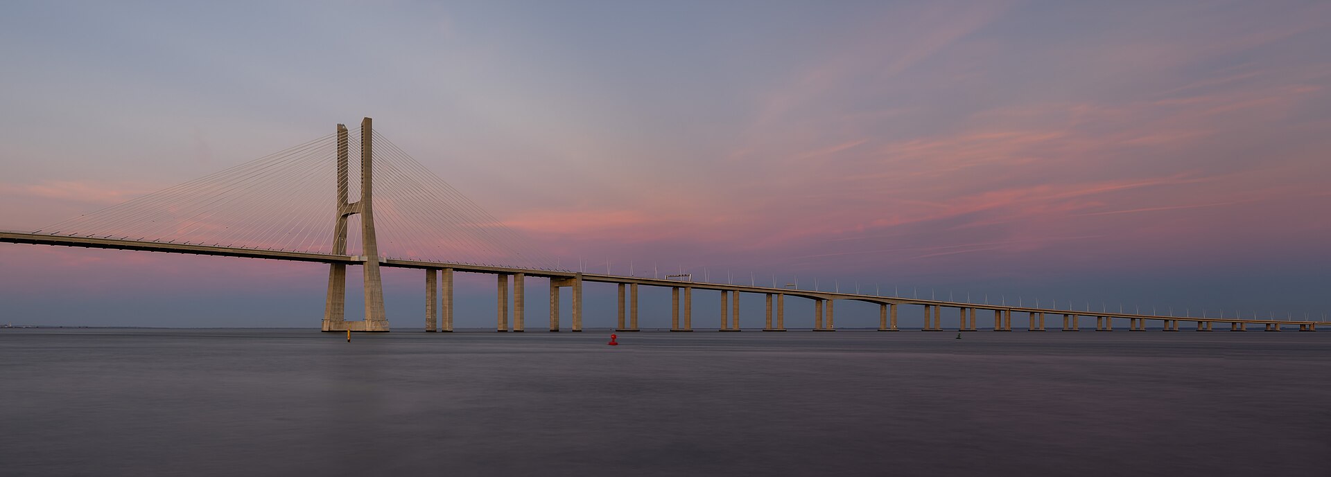 Ponte Vasco da Gama sobre o Tejo ao entardecer, com pilares refletidos na água.