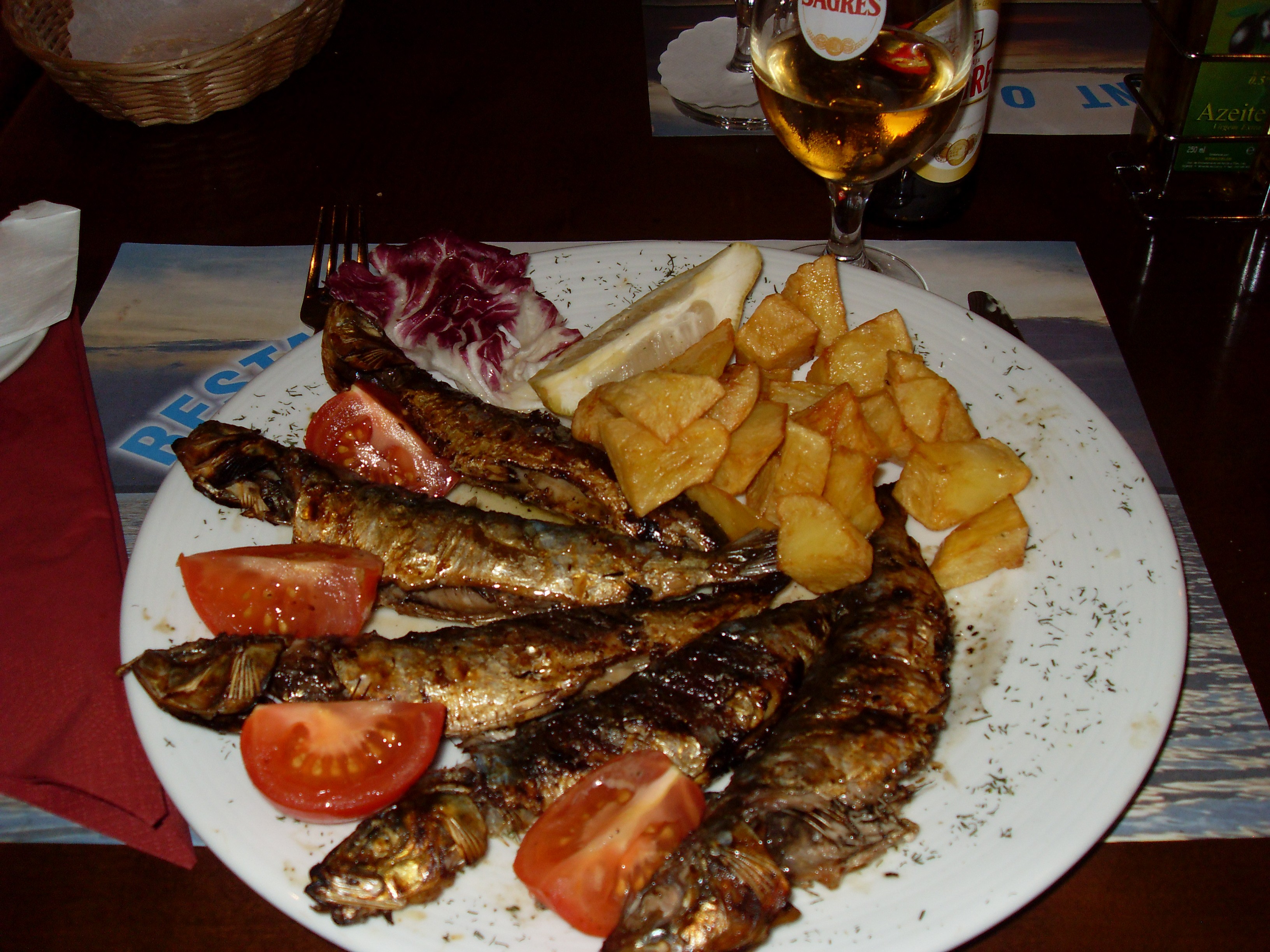 Sardinhas assadas em um prato com batatas, tomate e limão.